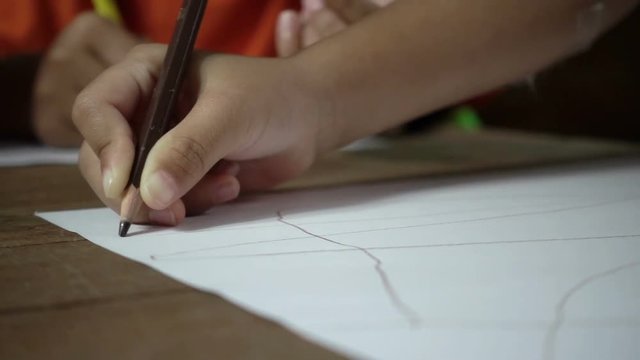 Little asian girl writing on desk in dark room, slow motion shot.