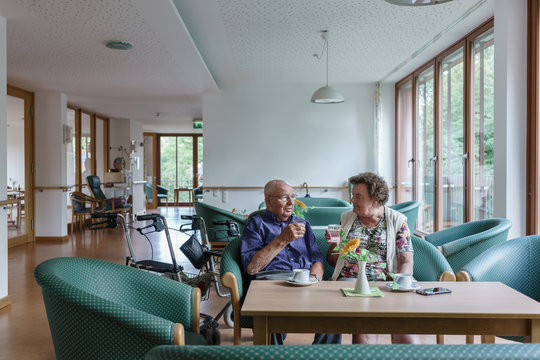 Man and woman, both seniors, couple, sitting on couch in retirement home having coffee