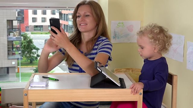 Young pretty woman taking photos of her daughter and herself with smart phone