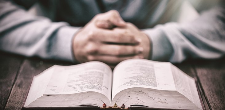 Man with bible praying at wooden table