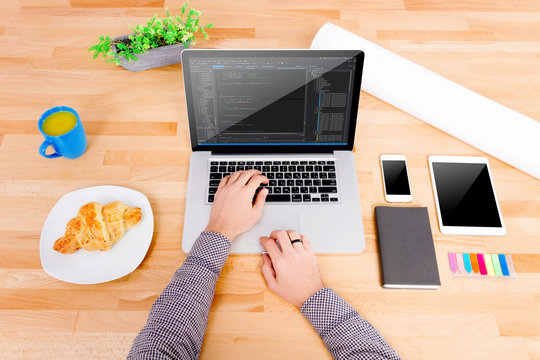 Software engineer's workplace with laptop, tablet, mockup smartphone, blue cup, croissant. The engineer working on the laptop. Note: Code was got from github with free license for commercial use (MIT)