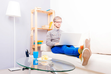 Guy wearing glasses sitting on the white couch and working on the laptop at home. Freelance concept.