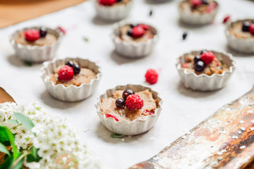 Raw dough with berries for cupcakes decomposed into forms on a baking papper on baking tray decorated ewith flowers. Selective focus. Vintage concept.