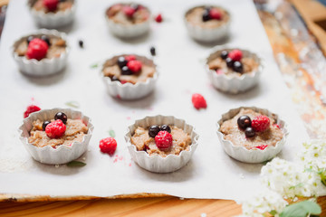 Raw dough with berries for cupcakes decomposed into forms on a baking papper on baking tray decorated ewith flowers. Selective focus. Vintage concept.