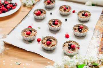 Raw dough with berries for cupcakes decomposed into forms on a baking papper on baking tray decorated ewith flowers. Selective focus. Vintage concept.