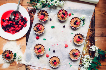 Top view Raw dough with berries for cupcakes decomposed into forms on a baking papper on baking tray decorated ewith flowers. Selective focus. Vintage concept, flatlay. Space for text