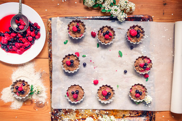 Top view Raw dough with berries for cupcakes decomposed into forms on a baking papper on baking tray decorated ewith flowers. Selective focus. Vintage concept, flatlay. Space for text