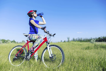 Naklejka premium Attractive, healthy woman drinks from her water bottle on mountain bike. active outdoor lifestyle concept.