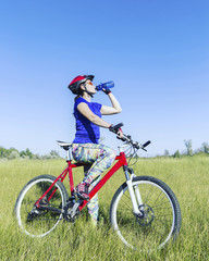 Naklejka premium Attractive, healthy woman drinks from her water bottle on mountain bike. active outdoor lifestyle concept.