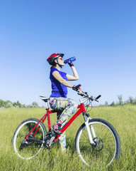 Plakat Attractive, healthy woman drinks from her water bottle on mountain bike. active outdoor lifestyle concept.