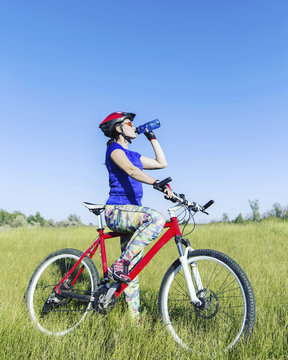 Attractive, healthy woman drinks from her water bottle on mountain bike. active outdoor lifestyle concept.
