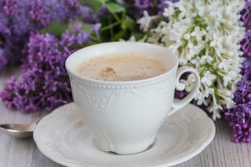 Fototapeta na wymiar spring coffee break with cup of coffee and different lilac flowers on light wooden background