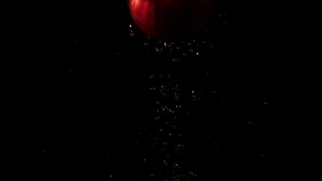 Red pomegranate goes down and up in aquarium standing on black background