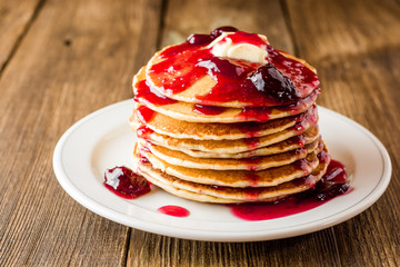 Pancakes with butter and jam on wooden table.