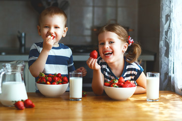 Happy children brother and sister eating strawberries with milk