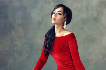 Fashion portrait of stylish brunette girl wearing red velvet dress Woman with ponytail hair wearing...