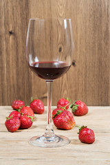 Glass with red wine on a wooden table with scattered ripe strawberries