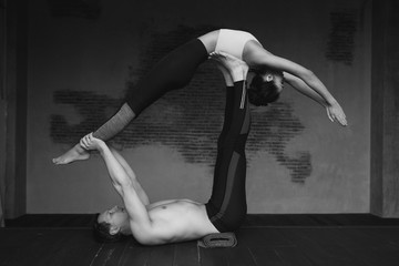 Young caucasian couple practice acroyoga in loft interior. Sporty handsome man supporting and holding slim beautiful brunette woman. Acro yoga concept showing strength and trust