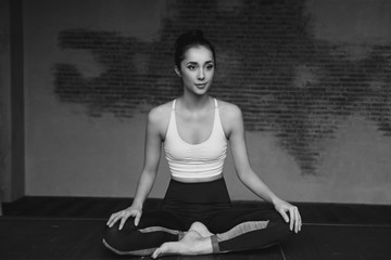 Young beautiful tanned woman practising yoga and relaxing in lotus position on yoga mat in loft interior