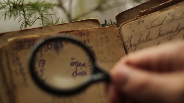 Hands searching in a vintage manuscript with magnifying glass.