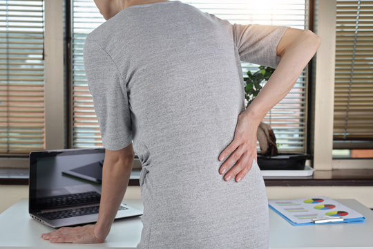 Business woman with back pain in an office . Pain relief concept