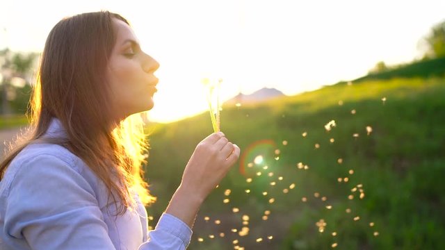 Beauty woman blowing dandelion against the sunset, slow motion
