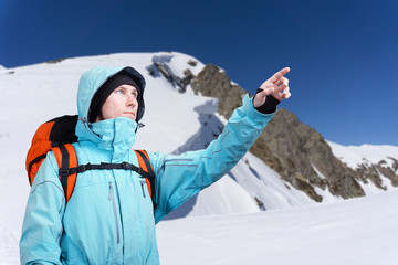 The mountaineer pointing at peak, standing against a winter mountain landscape.