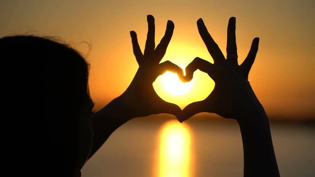 Woman makes heart and hands directs the sunset