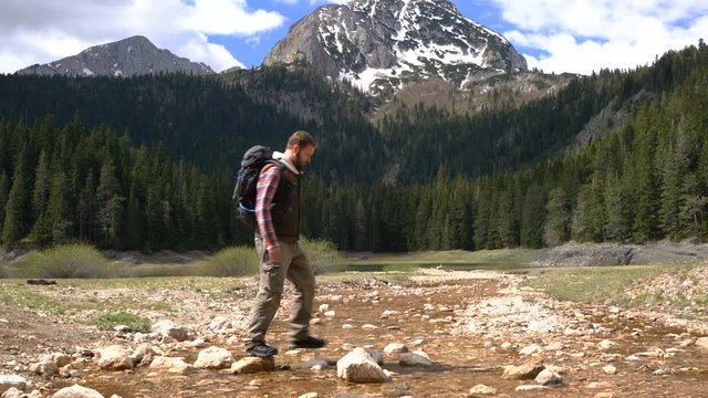 Traveler with a backpack crosses a creek stepping on stones