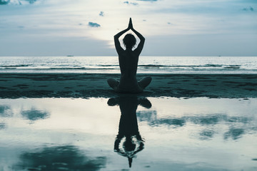 Yoga woman silhouette on sea coast at twilight. Reflection in the water.