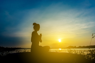 Silhouette beautiful women yoga in nature on the rock and river over sunset background.