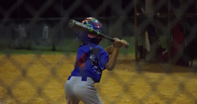 Slow motion of kid batting and running to first base at baseball game