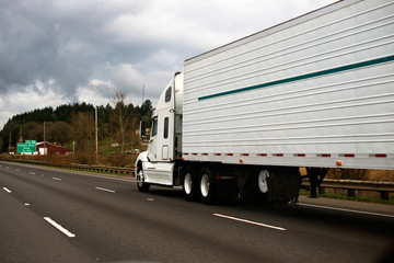 Big modern white semi truck trailer reefer on wide highway
