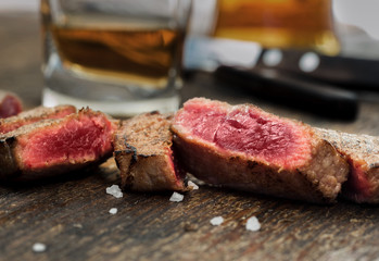 Sliced grilled beef steak on wooden table with whiskey