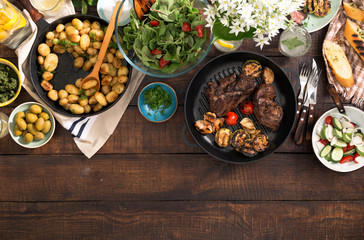 Grilled steak, vegetables, potatoes, salad, snacks, lemonade on wooden table