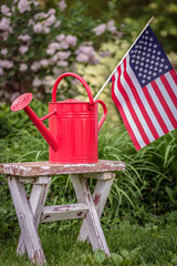 Red watering can with American flag on shabby white potting bench in garden © Kristen