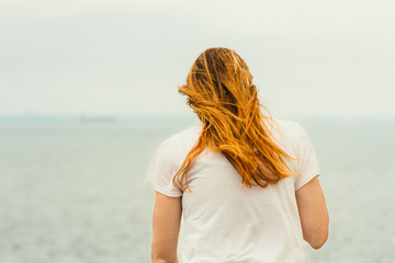 Young redhead woman sitting in front of the sea view from back