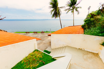 Woman sitting on a bench on an esplanade facing the sea next to palm trees