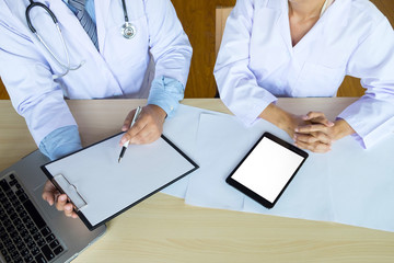 Two doctors discussing patient notes in an office pointing to a clipboard with paperwork as they make a diagnosis or decide on treatment