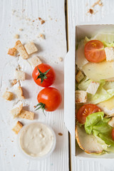 Caesar salad in box on white wooden surface