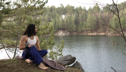 Young guy sits on high bank above lake.