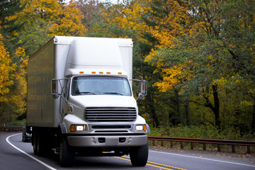 Middle size semi truck with box cargo on twisted highway