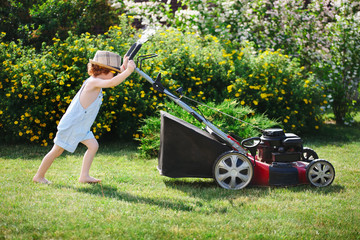 little boy mows lawn with mower