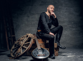 Portrait of musician dressed in old Celtic clothes sits on a wooden box and performing old mandolin.