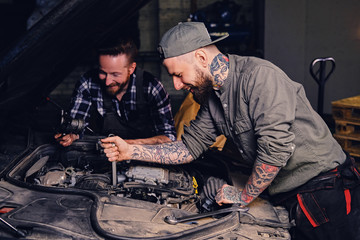 Two mechanics fixing car's engine in a garage.