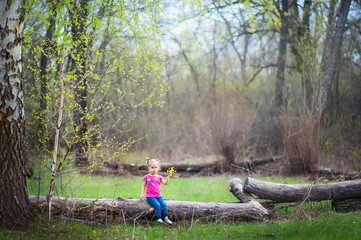 Beautiful little girl on a walk in the park in spring, summer. The girl walks through the woods, resting, having fun. A child in a pink blouse and jeans. Girl with funny tails. The girl knows the worl