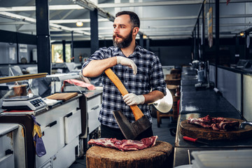 Portrait of a butcher holds an axe and fresh cut meat.