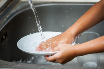 Fototapeta premium Child hand washing dishes over the sink in the kitchen