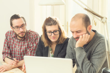 Group of ordinary young people discussing business plans, with lap-tops, plans in a room lit by natural sunlight.