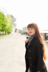 Beautiful red-haired young woman walking down the embankment on a sunny day, examining the neighborhood.